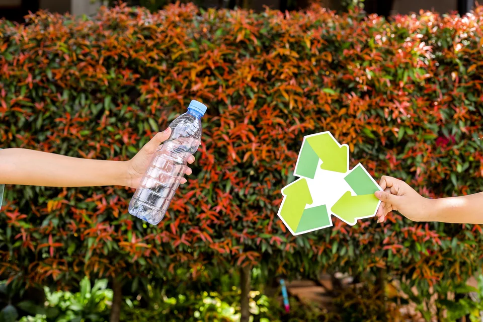 Hands holding a plastic bottle and recycling sign